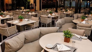 Un restaurante con mesas redondas y asientos acolchados, algunos con plantas.