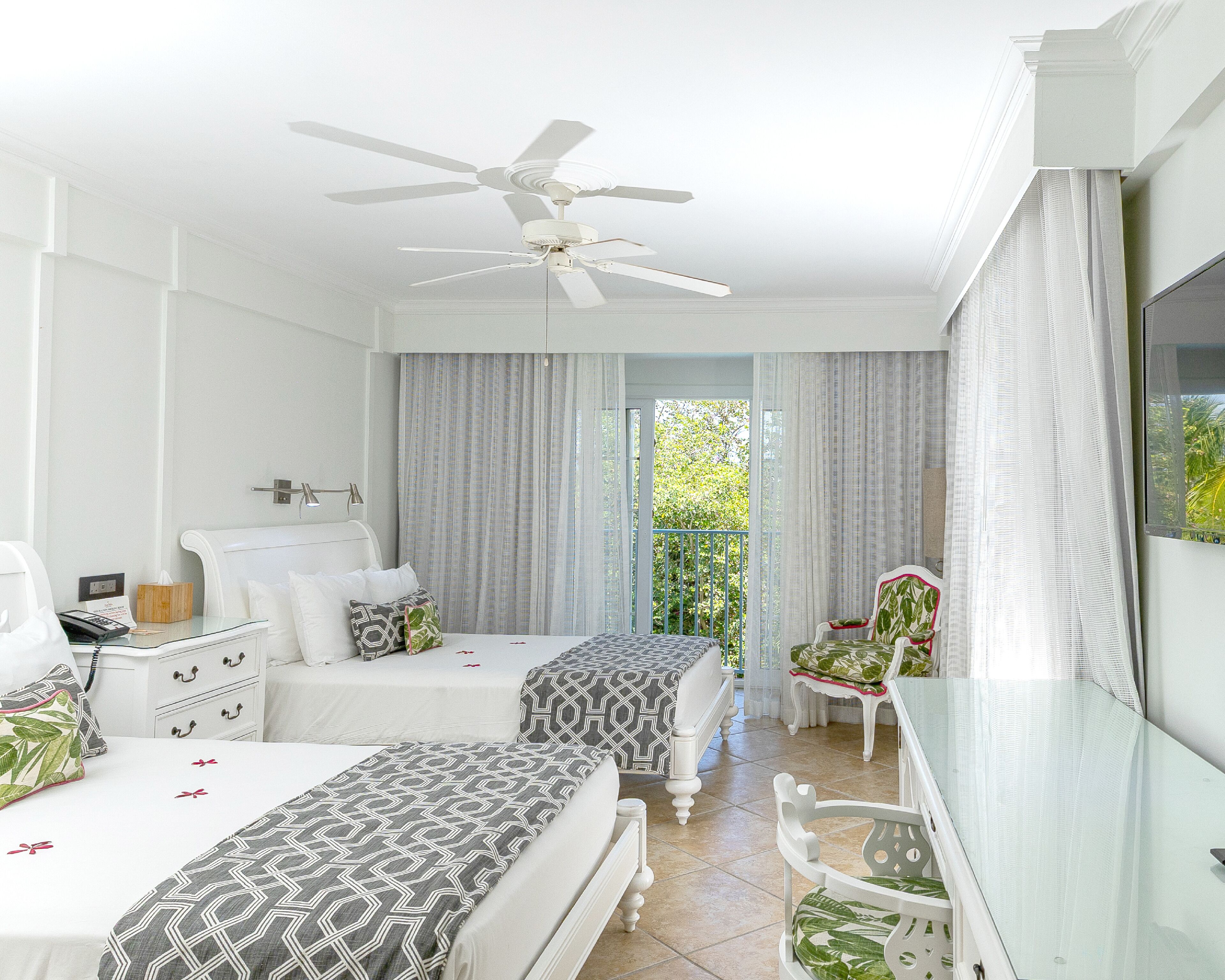 A hotel room with two beds, a ceiling fan, a desk with a telephone, and a chair.