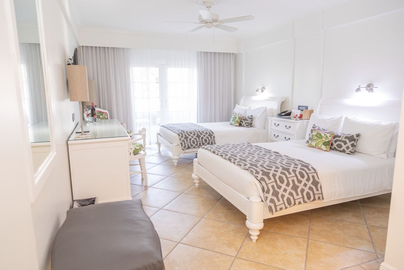 Habitación de hotel con dos camas, un escritorio, una silla, un armario y un ventilador de techo.
