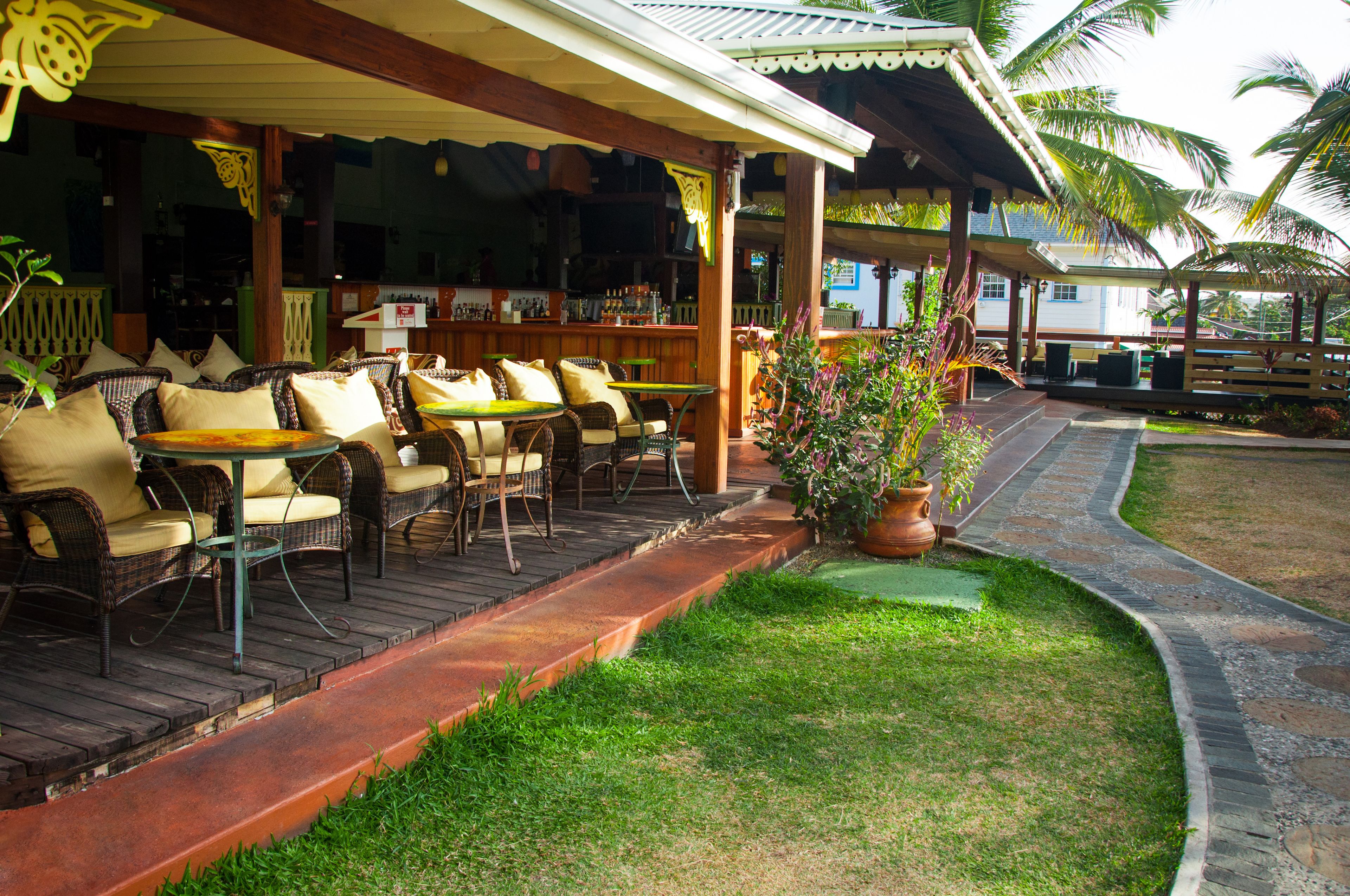 A covered outdoor seating area with wicker furniture and a bar in the background.