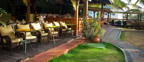 A covered outdoor seating area with wicker furniture and a bar in the background.