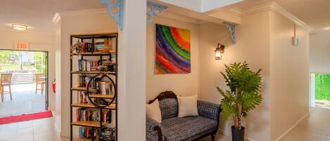A spacious lobby with a bookshelf, a colorful abstract painting, a seating area with a patterned sofa, and a potted plant.