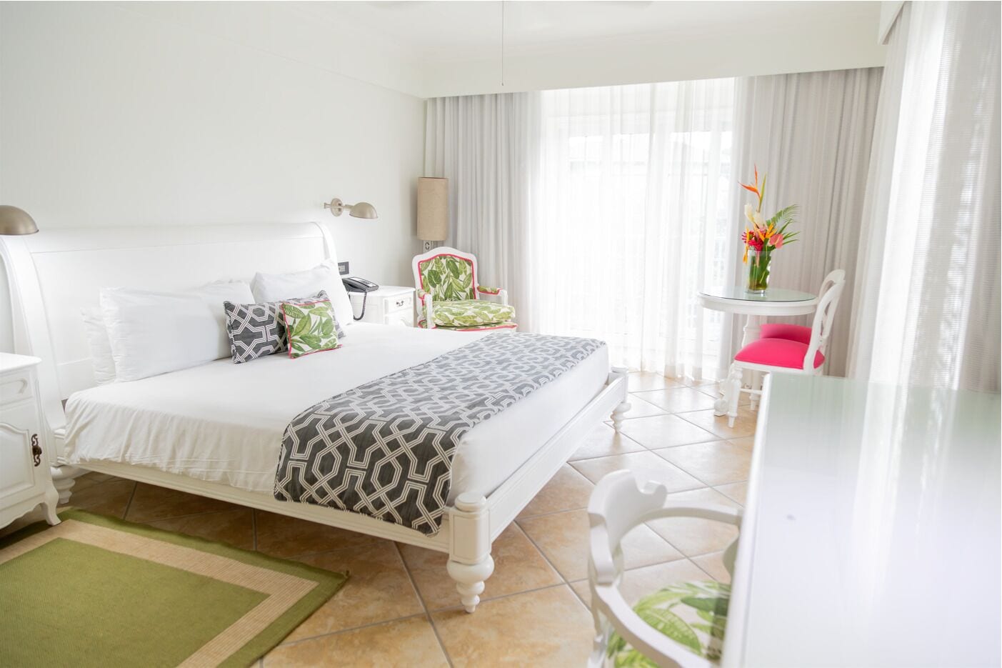 A hotel room with a large bed, a desk, a chair, and a small table with a vase of flowers.