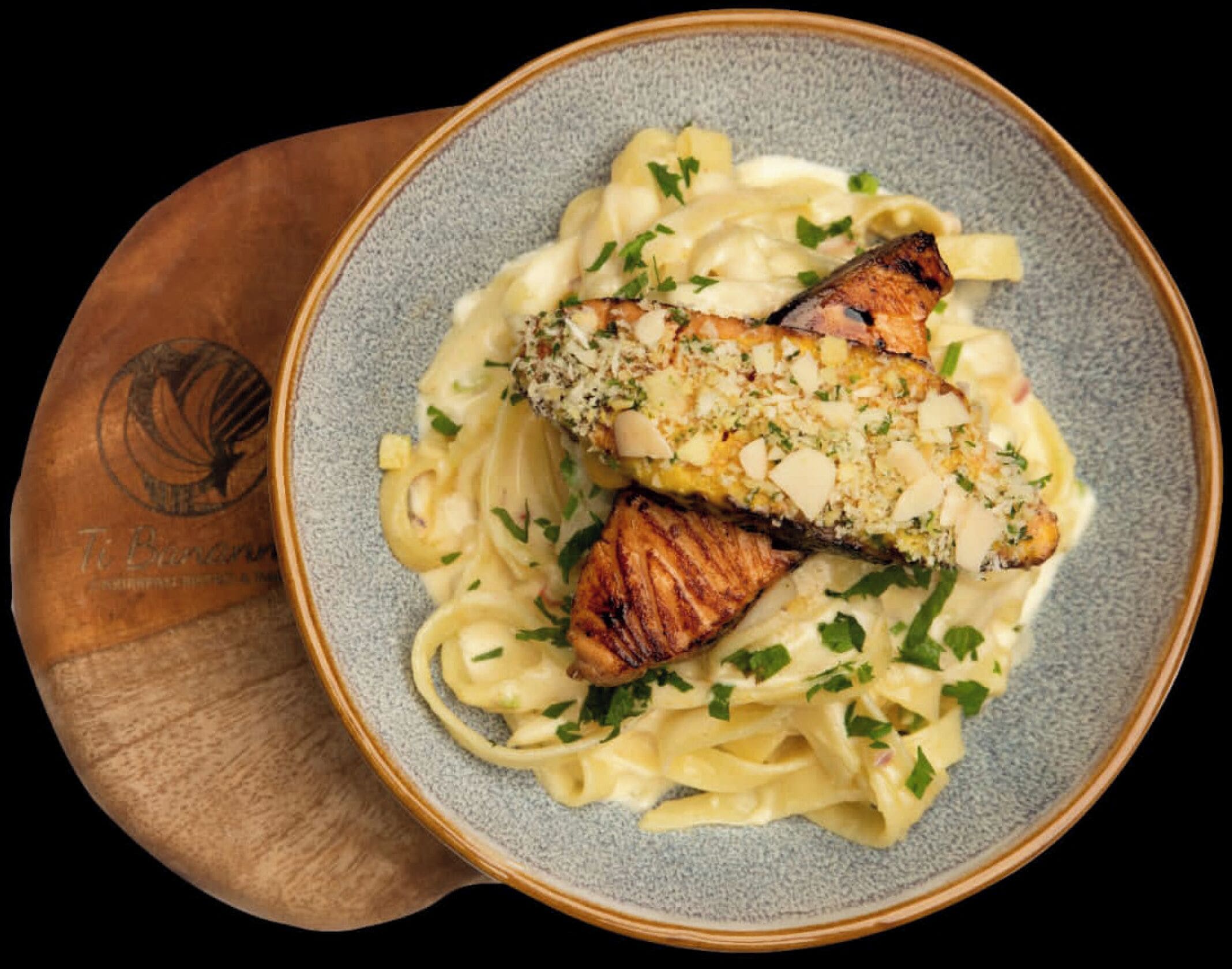 A plate of pasta with a grilled fish topping, garnished with herbs.