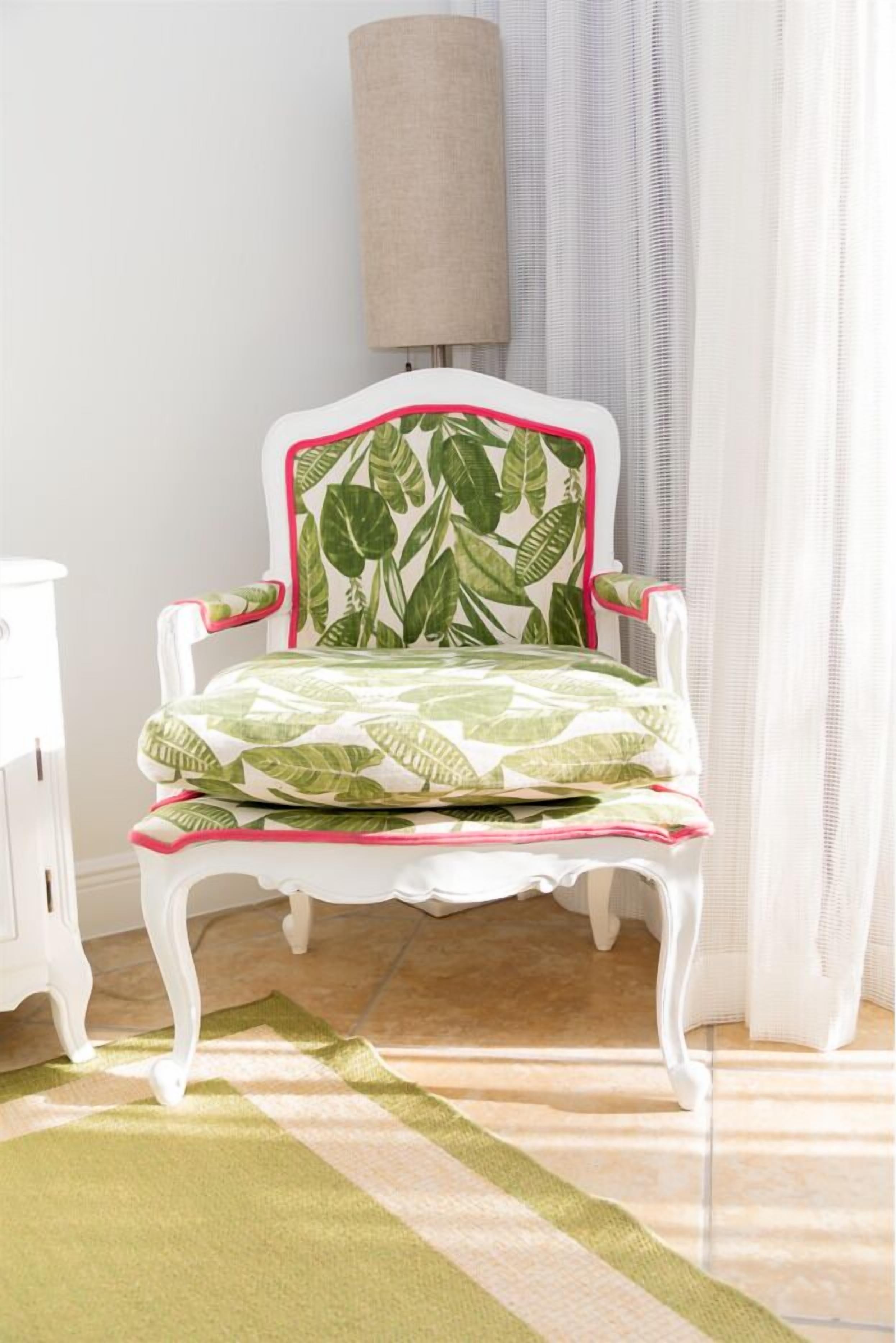 A white chair with a green leaf pattern and pink trim, placed on a striped rug.