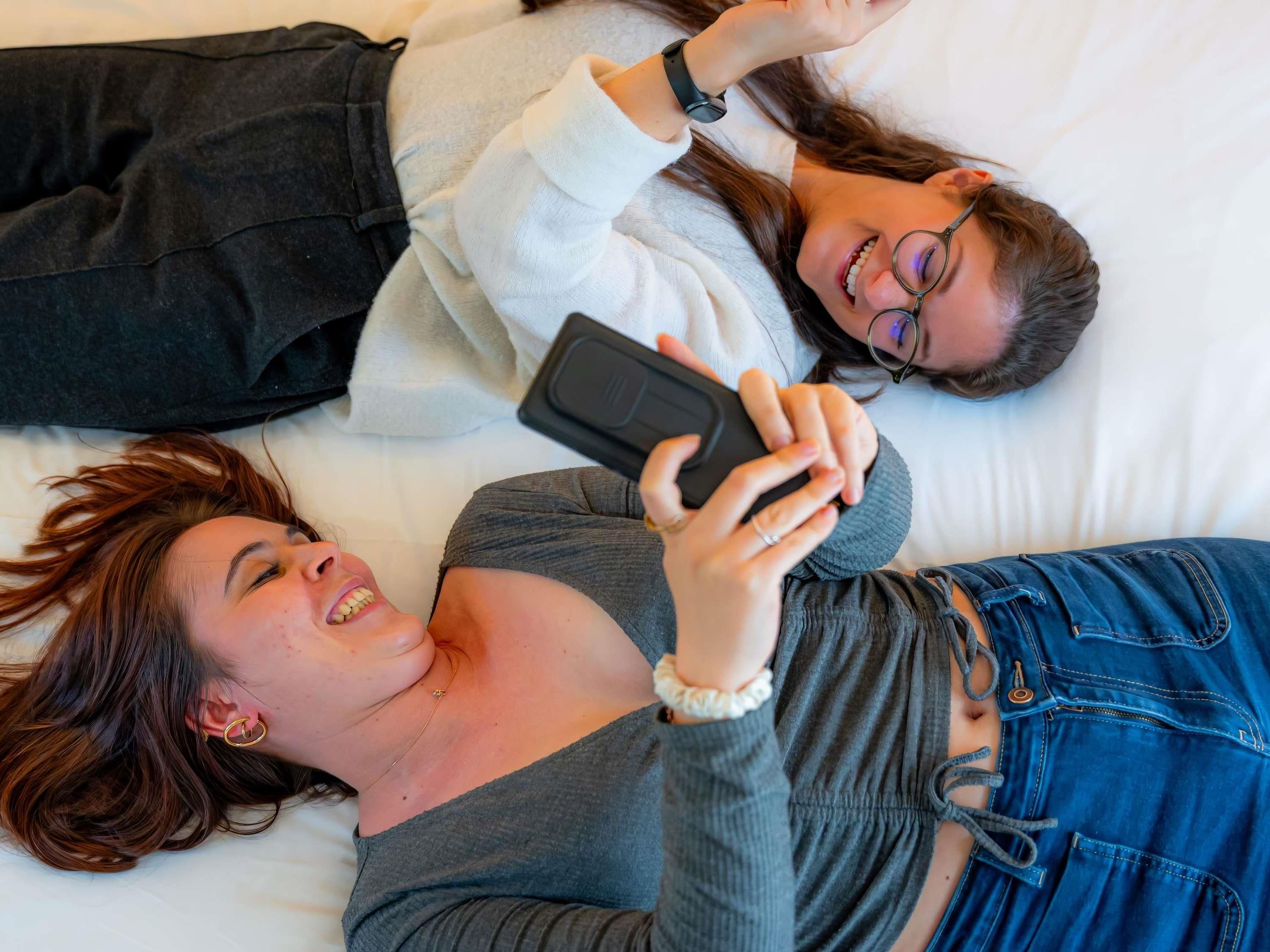 Dos personas recostadas sobre una cama con un almohadón blanco y una manta negra.