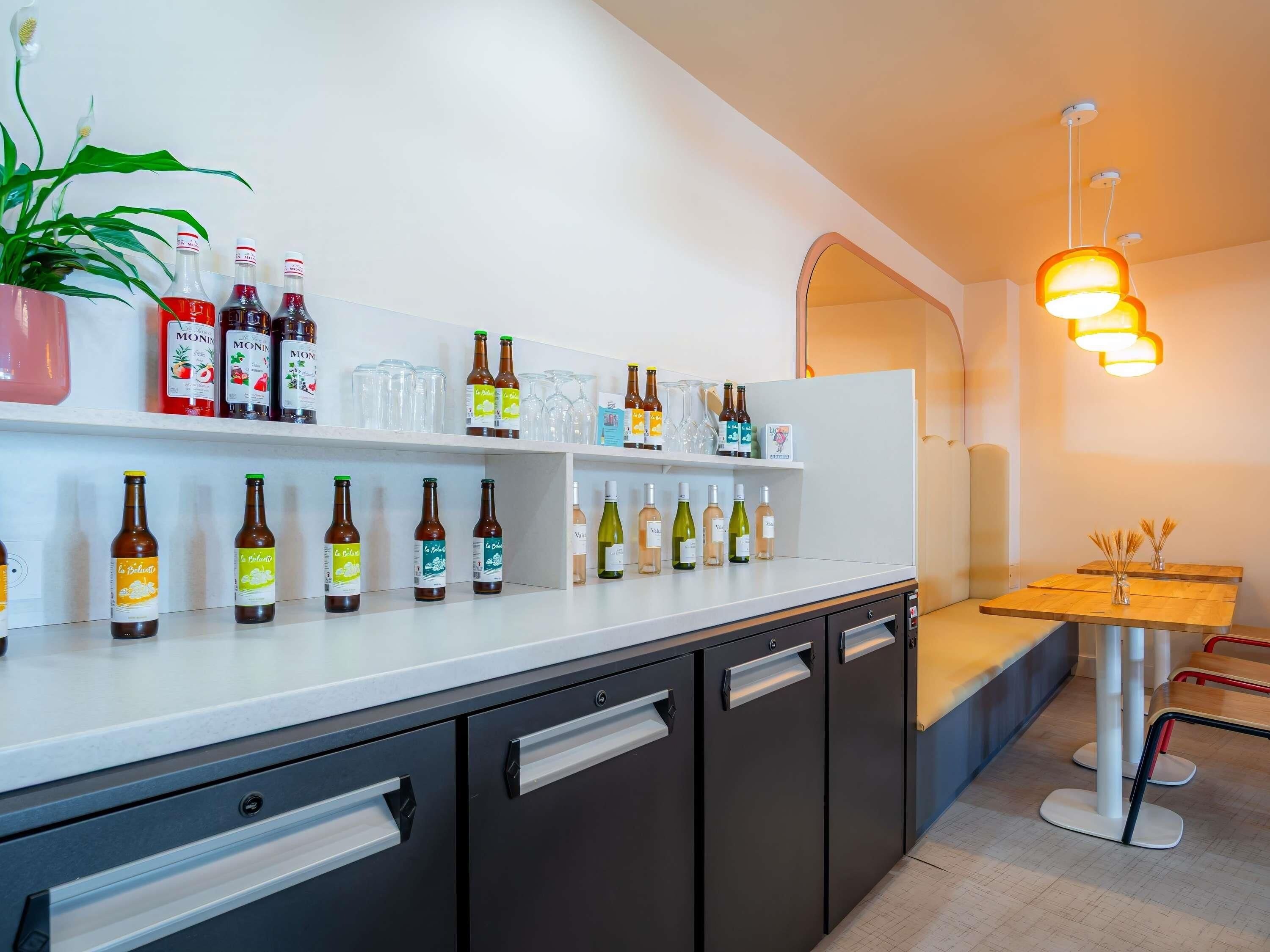 A modern bar area with shelves of bottled beverages, a potted plant, and a seating area with a wooden table and chairs.