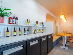 A modern bar area with shelves of bottled beverages, a potted plant, and a seating area with a wooden table and chairs. - ibis Styles Nantes Centre Place Graslin (Nantes)