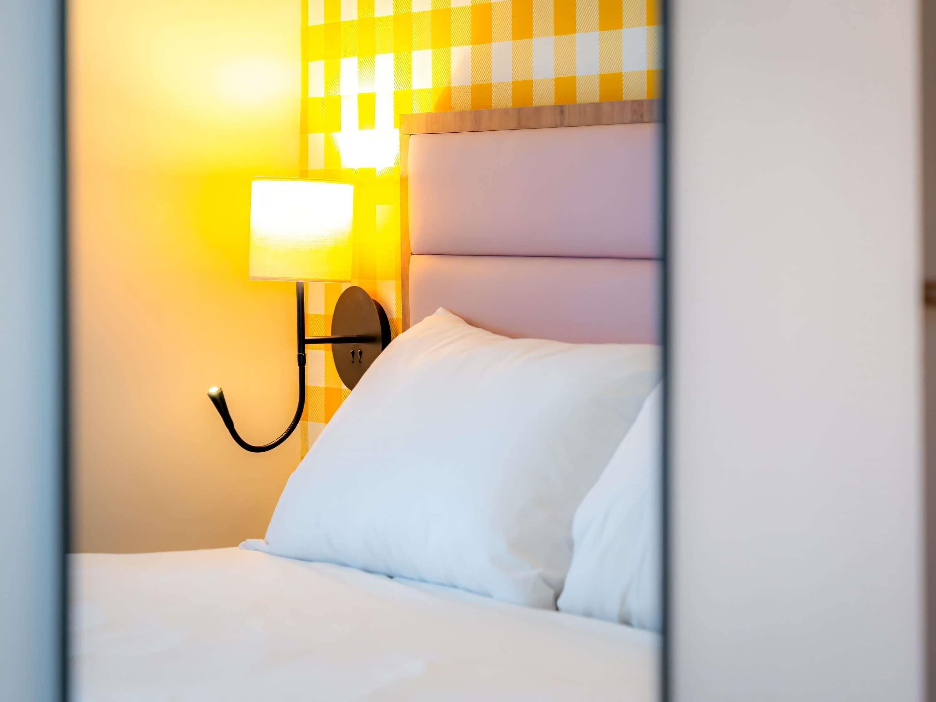 A hotel room with a bed, a wall-mounted lamp, and a checkered wall pattern.