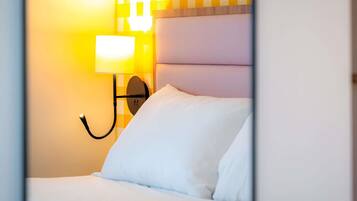 A hotel room with a bed, a wall-mounted lamp, and a checkered wall pattern.