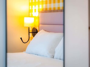 A hotel room with a bed, a wall-mounted lamp, and a checkered wall pattern. - ibis Styles Nantes Centre Place Graslin (Nantes)
