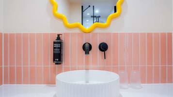 Un baño con un lavamanos blanco, un espejo con marco amarillo, una botella de champú y dos grifos negros.