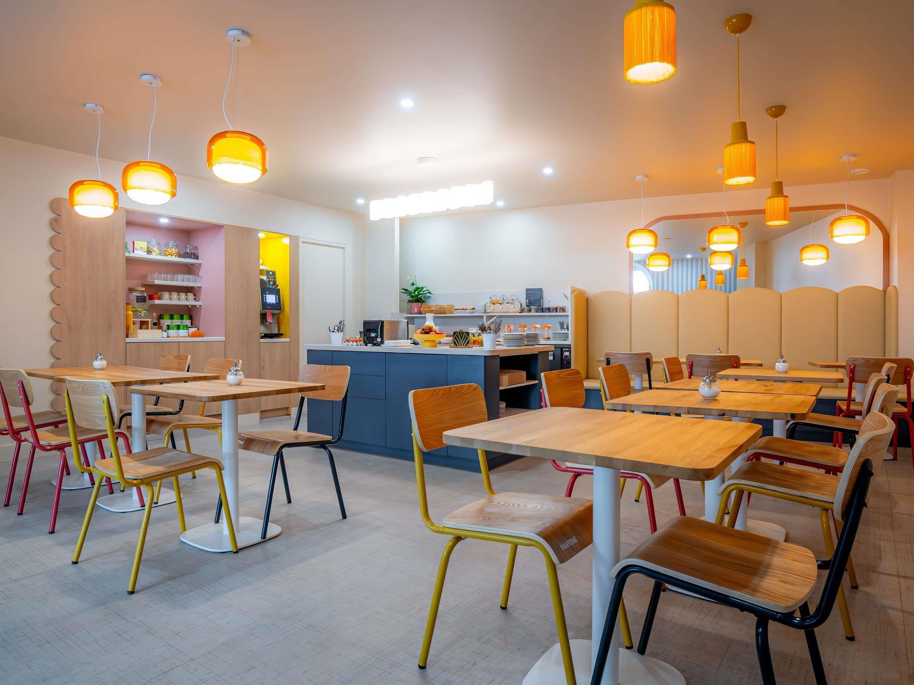A modern dining area with wooden tables and chairs, a central counter, and pendant lighting.