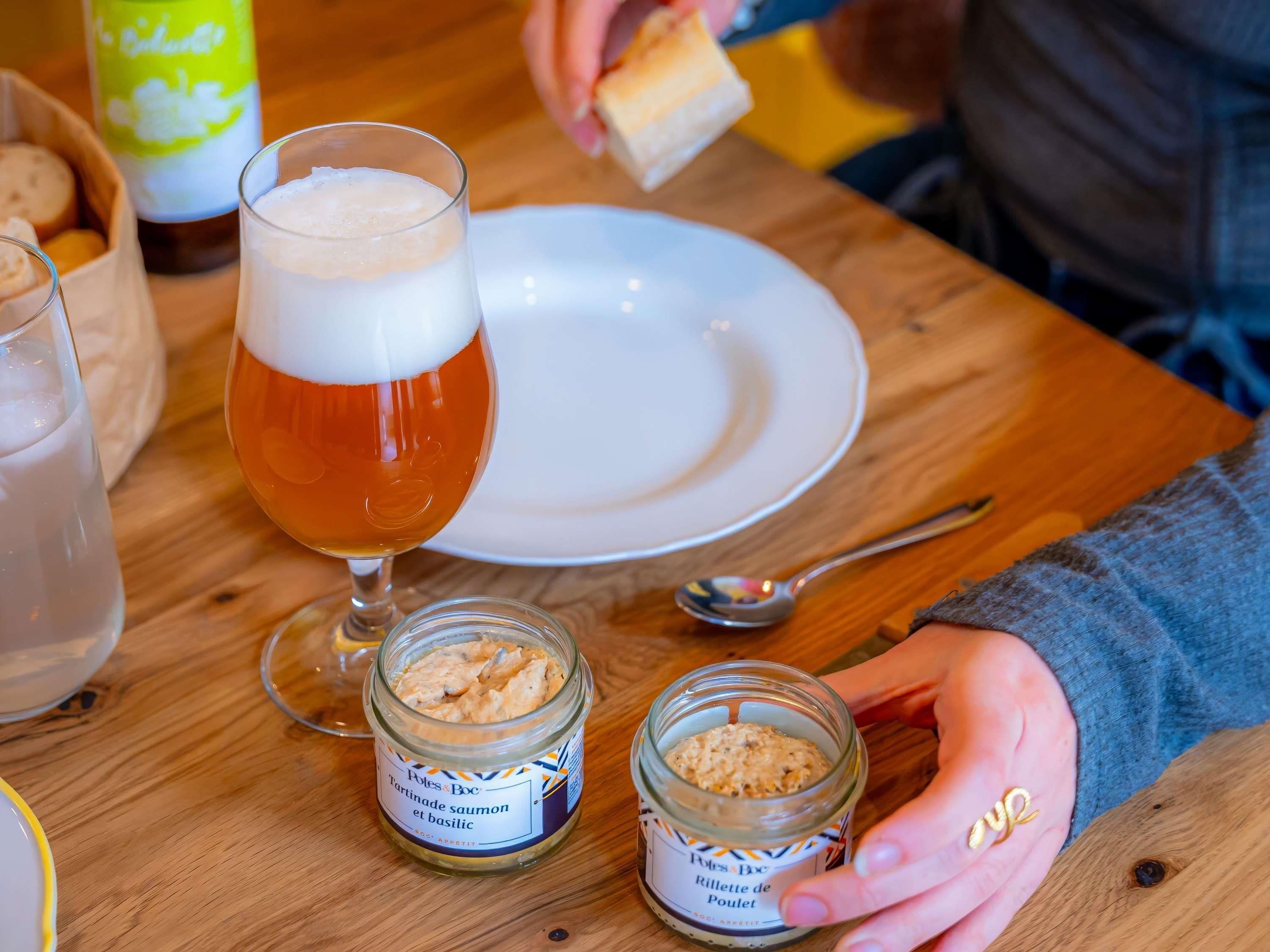 A wooden table with a glass of beer, a plate, and two jars of food.
