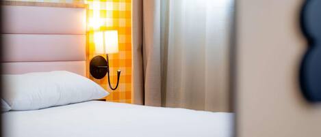 Ein Hotelzimmer mit karierter Wand, einem Bett mit weißer Bettwäsche und einer Wandlampe.