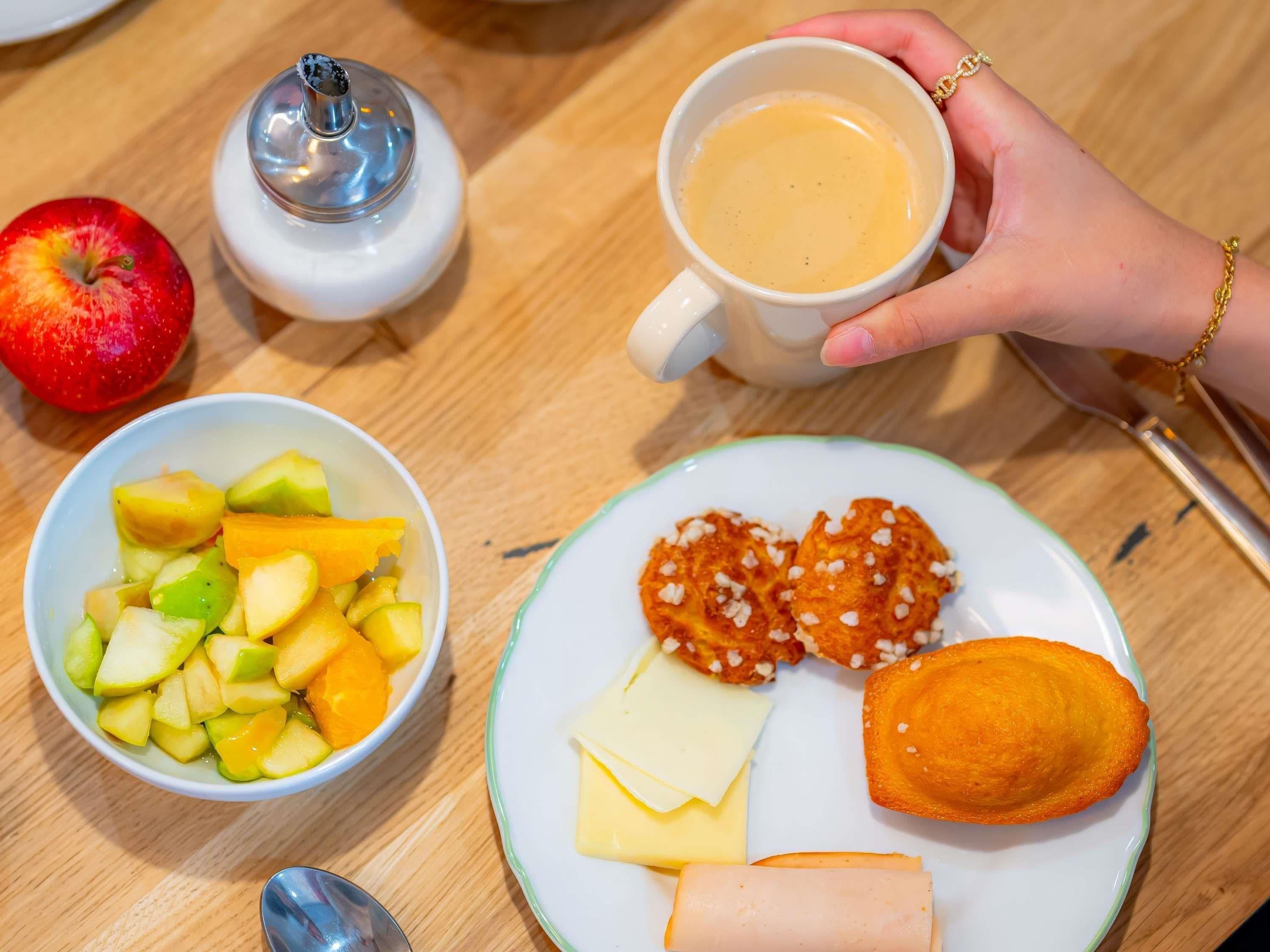 Een tafel met een bord eten, een schaal fruit, een kop koffie en een zilveren houder.