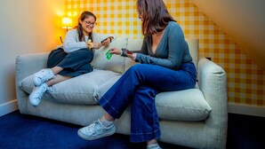 Two people sitting on a couch in a room with a checkered wall pattern and a sloped ceiling.