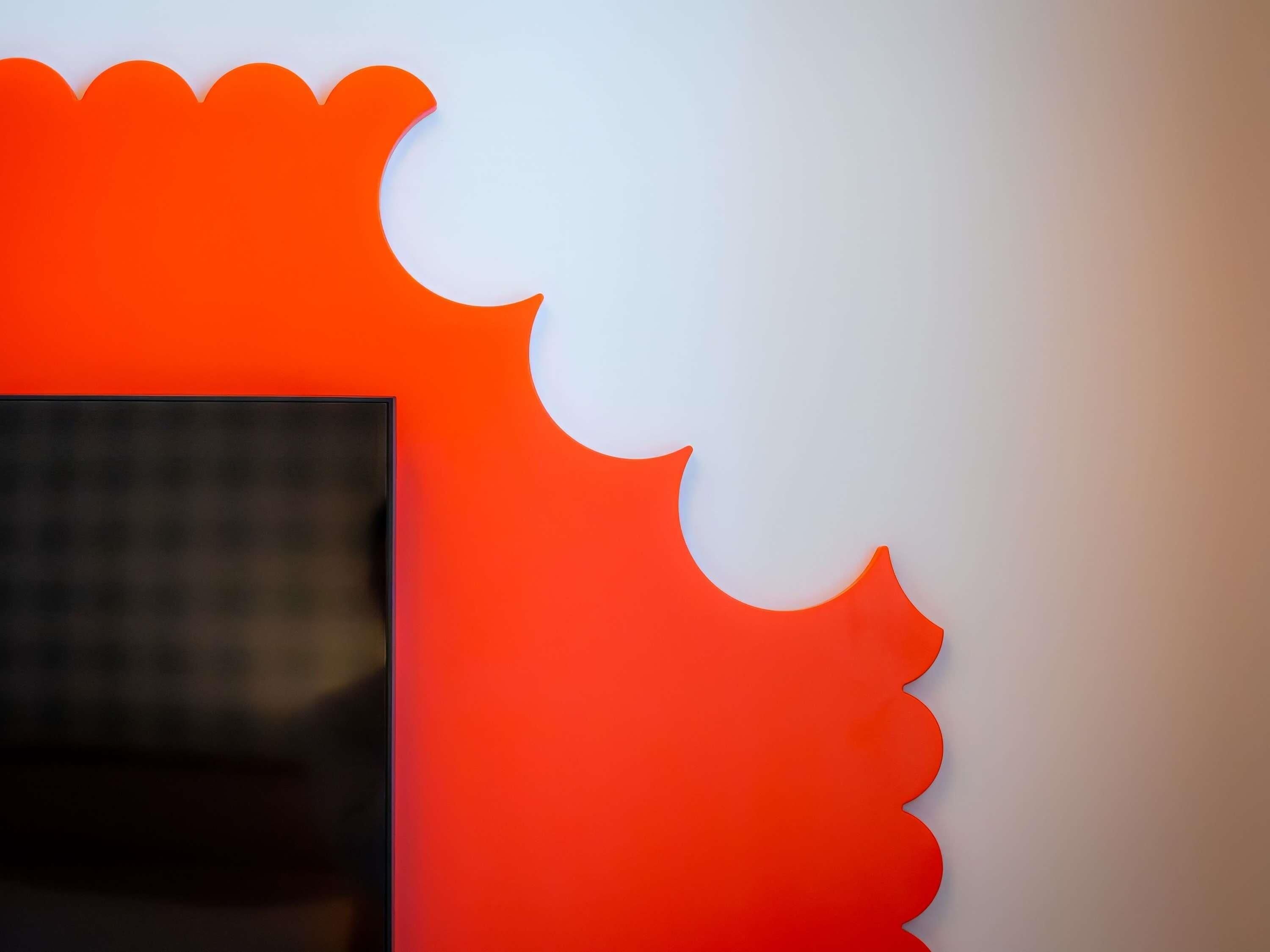 A wall with a large, partially obscured rectangular object, possibly a window or door, and a bright orange, scalloped design element.