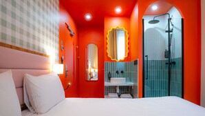 Habitación de hotel con cama, baño con ducha y espejo.