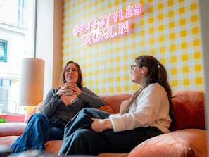 Two people sitting on a couch with a checkered wall and a neon sign in the background. - ibis Styles Nantes Centre Place Graslin (Nantes)