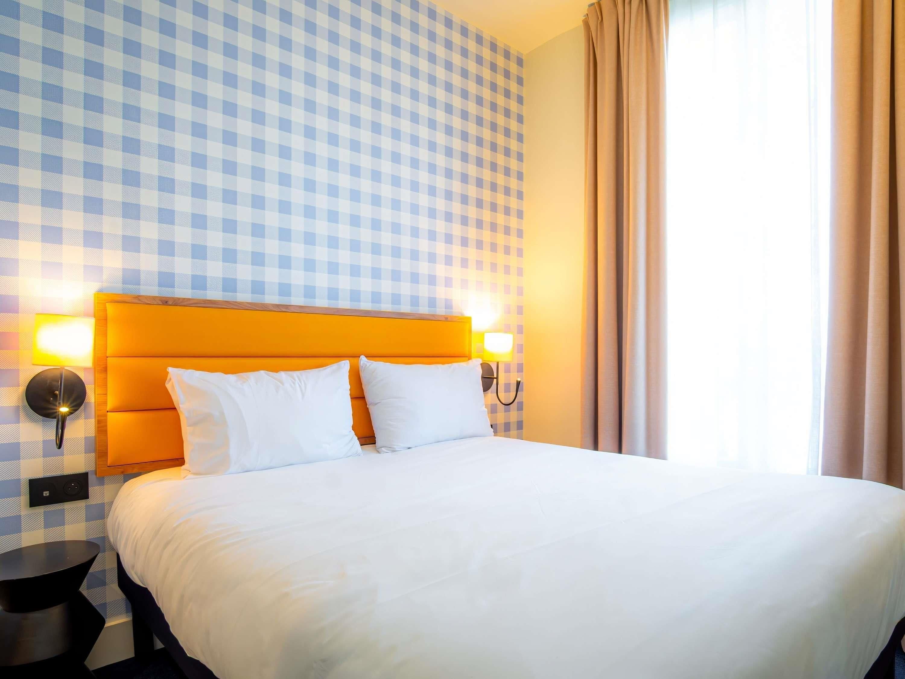 A hotel room with a checkered wall, a bed with white bedding, and two bedside lamps.
