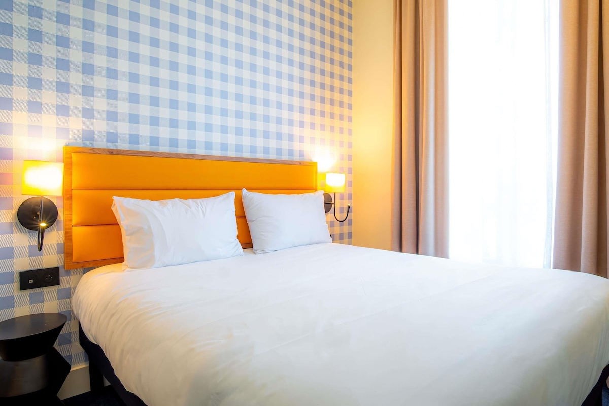 A hotel room with a checkered wall, a bed with white bedding, and two bedside lamps.