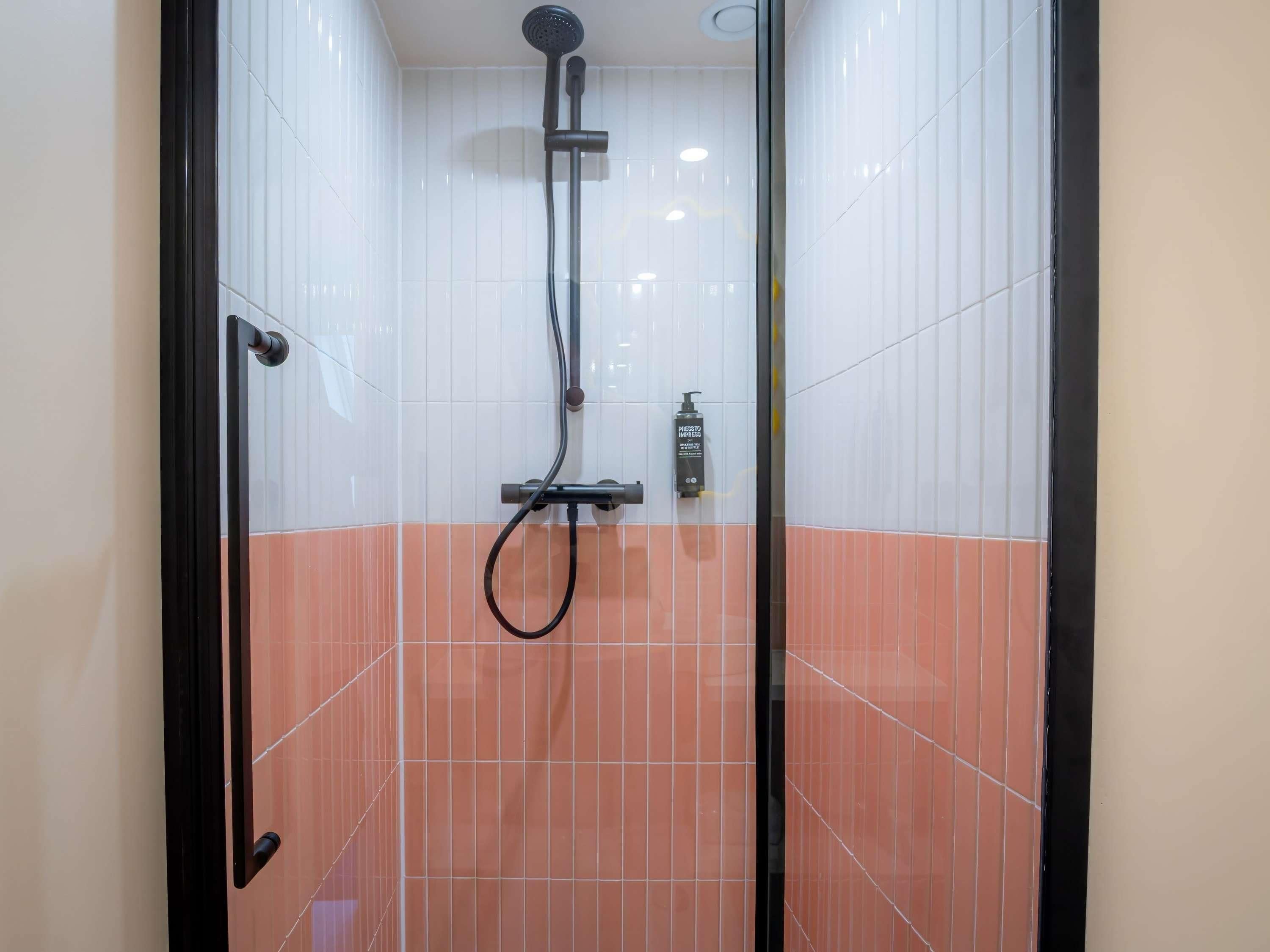 A shower area with white and orange tiles, a handheld showerhead, and a bottle of shampoo.