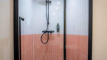 A shower area with white and orange tiles, a handheld showerhead, and a bottle of shampoo.