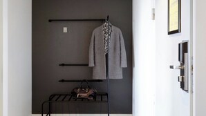 Una stanza con una parete grigia, un appendiabiti con un cappotto grigio e una sciarpa a leopardato, una borsa nera su uno scaffale e un menù incorniciato al muro.