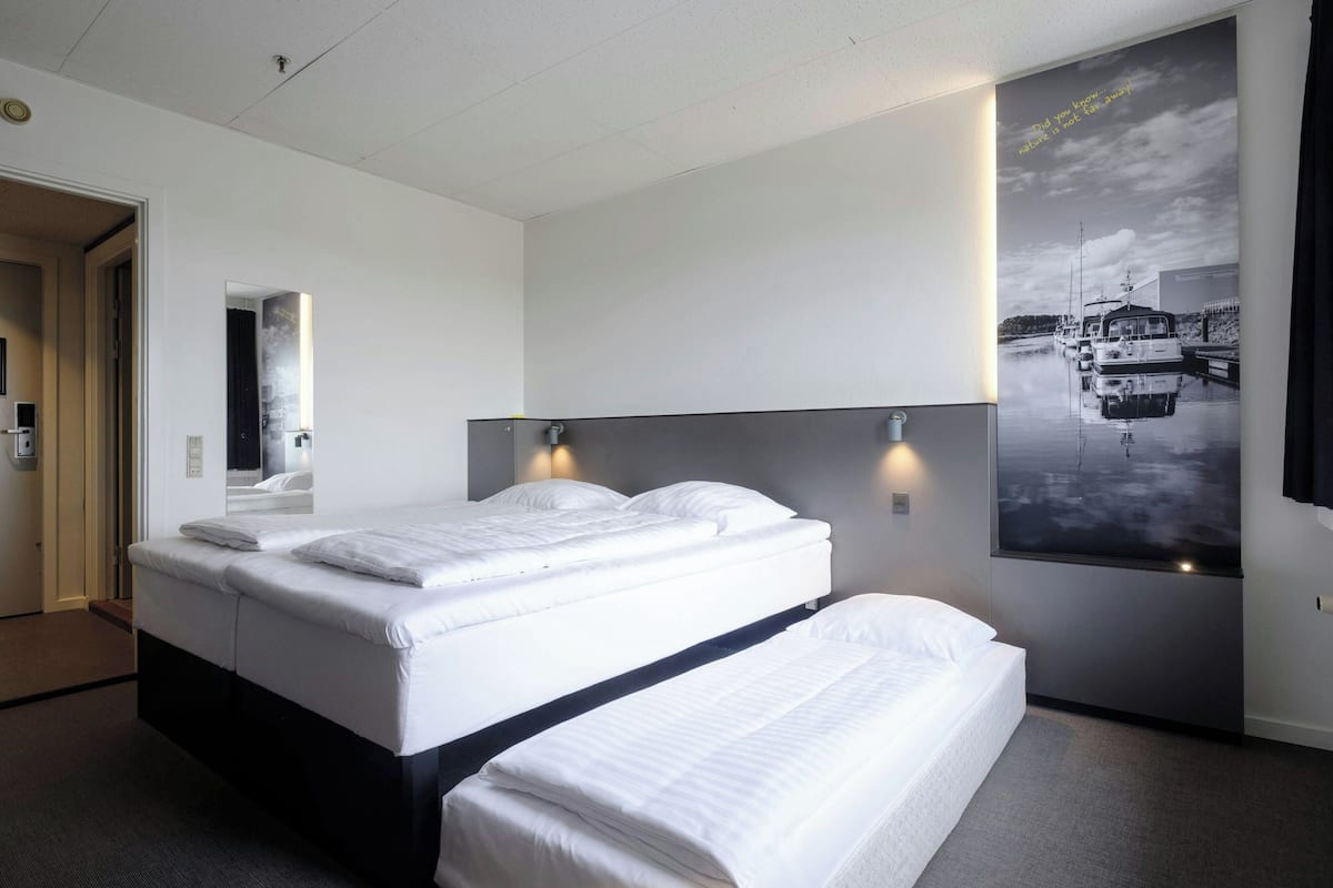 Hotellihuone, jossa on suuri sänky, pääty ja seinällä veneaiheinen juliste.