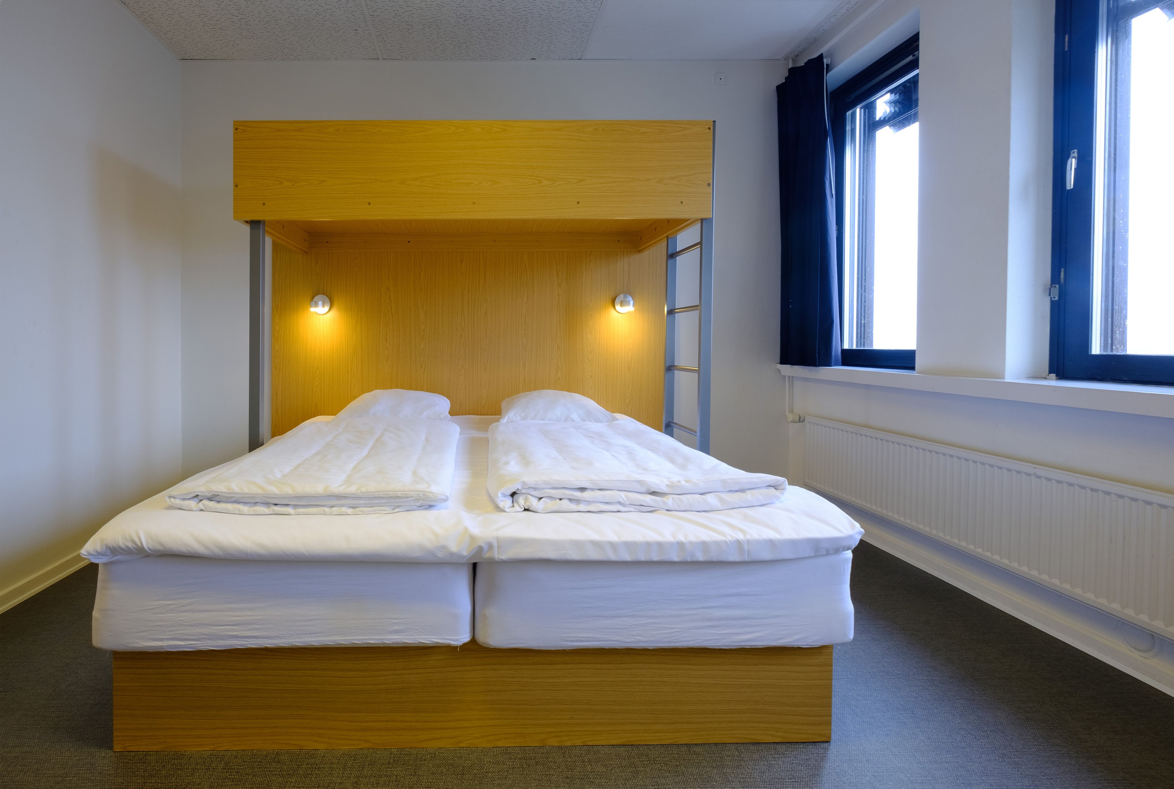 A double bed with a wooden headboard, two bedside lamps, and a window with curtains.