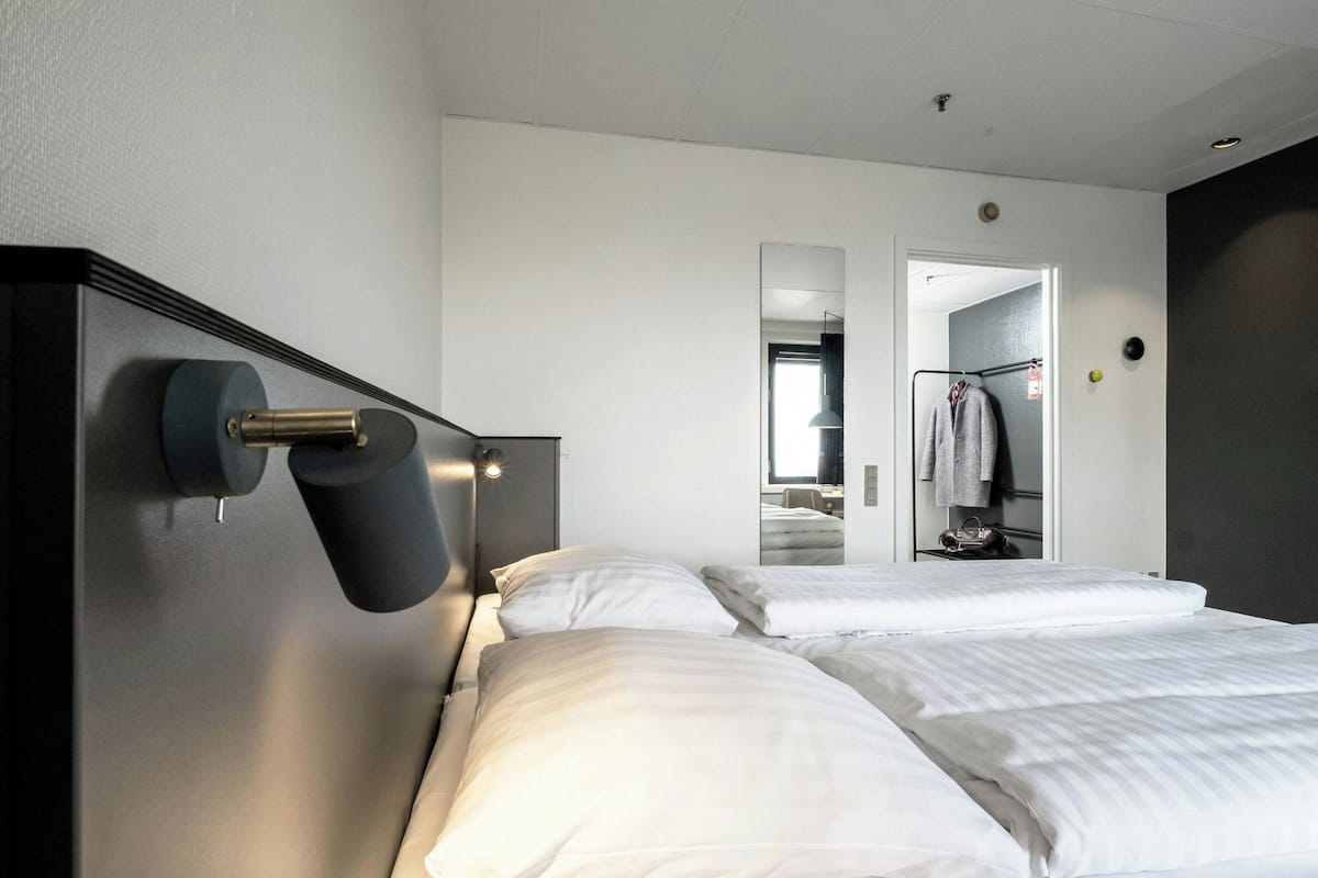Hotellihuone, jossa on suuri sänky, yöpöytä lampulla, peili ja vaatekaappi.