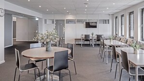 Una sala conferenze moderna con tavoli rotondi, sedie nere e piante in vaso.