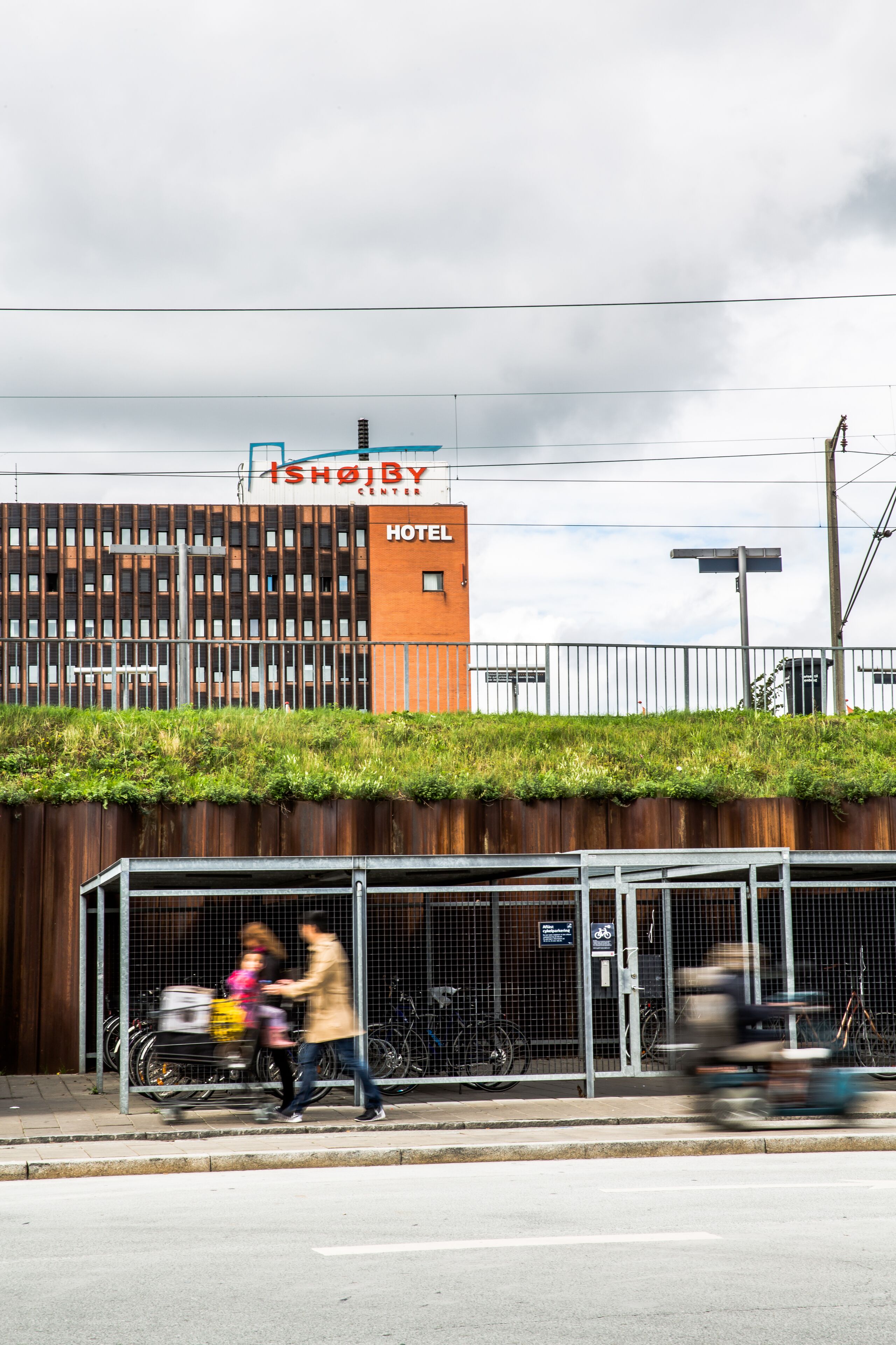 A hotel with a modern design, a visible sign for the Ishøjby Hotel, and a bike parking area.