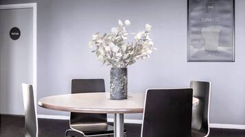 Une salle de conférence avec une table ronde, quatre chaises noires, un vase avec des fleurs blanches et une affiche encadrée au mur.