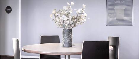 Un salón de conferencias con una mesa redonda, cuatro sillas negras, un jarrón con flores blancas y un cartel enmarcado en la pared.