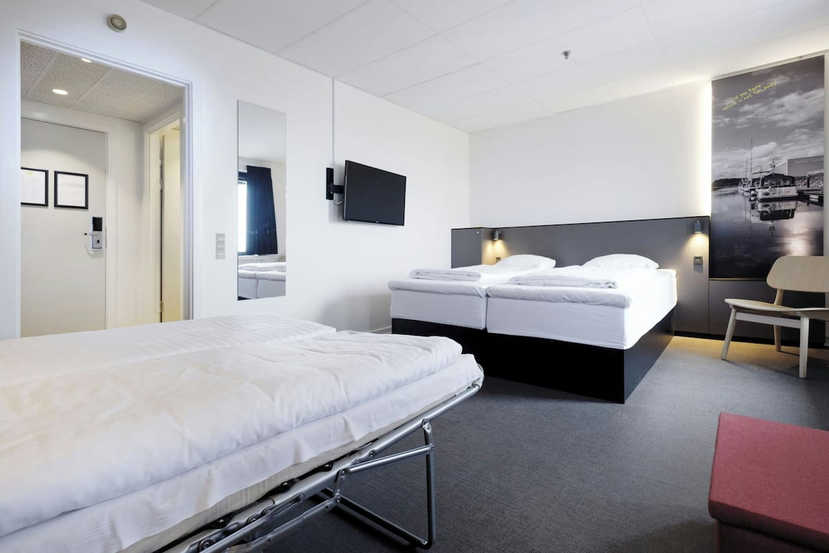 Moderni hotellihuone, jossa on suuri sänky, pienempi sänky, työpöytä ja tuoli.