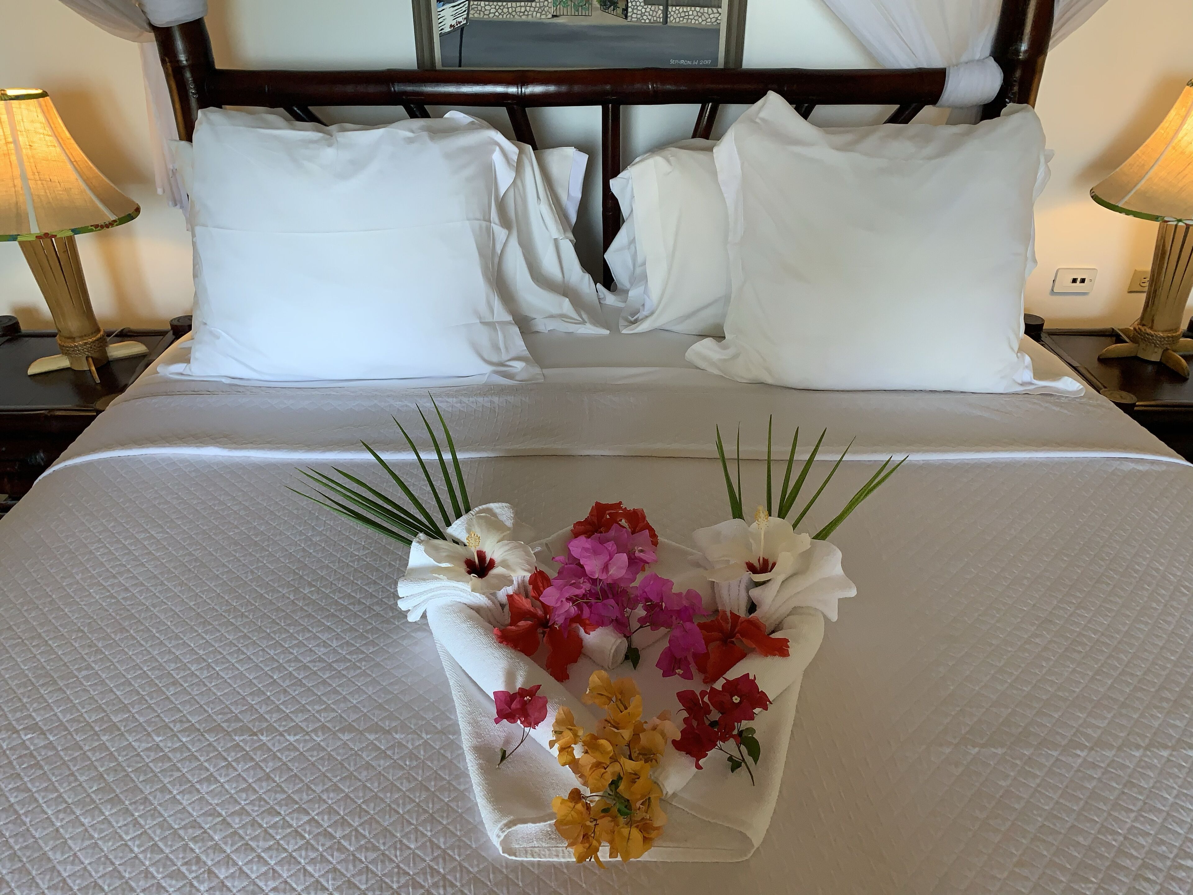 A neatly made bed with white linens and a floral centerpiece.