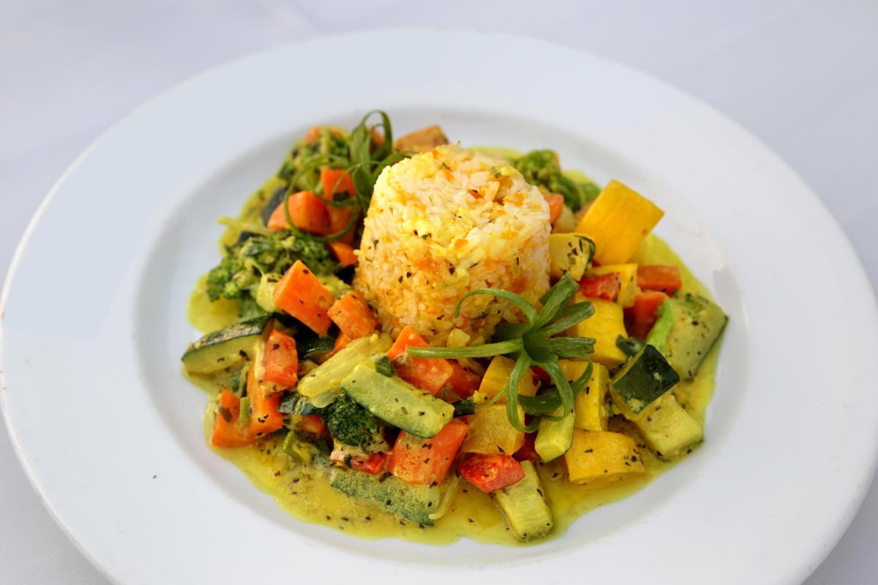 A plate of food with a mound of rice, various vegetables, and a garnish.
