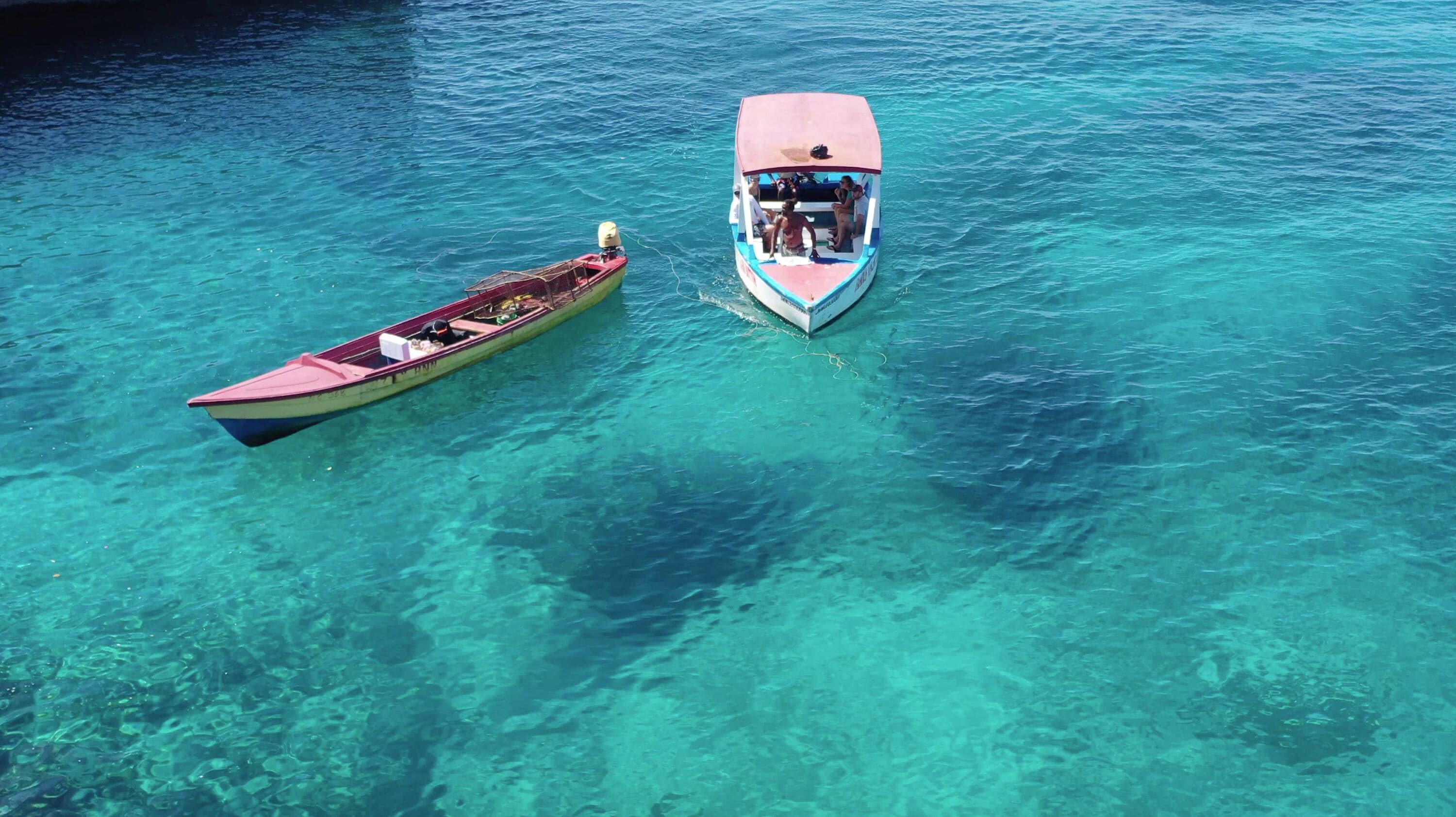 Dos barcos sobre aguas turquesas y transparentes.