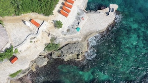 An aerial view of a coastal property with a rocky shoreline, clear blue waters, and several orange-roofed structures likely serving as accommodations.
