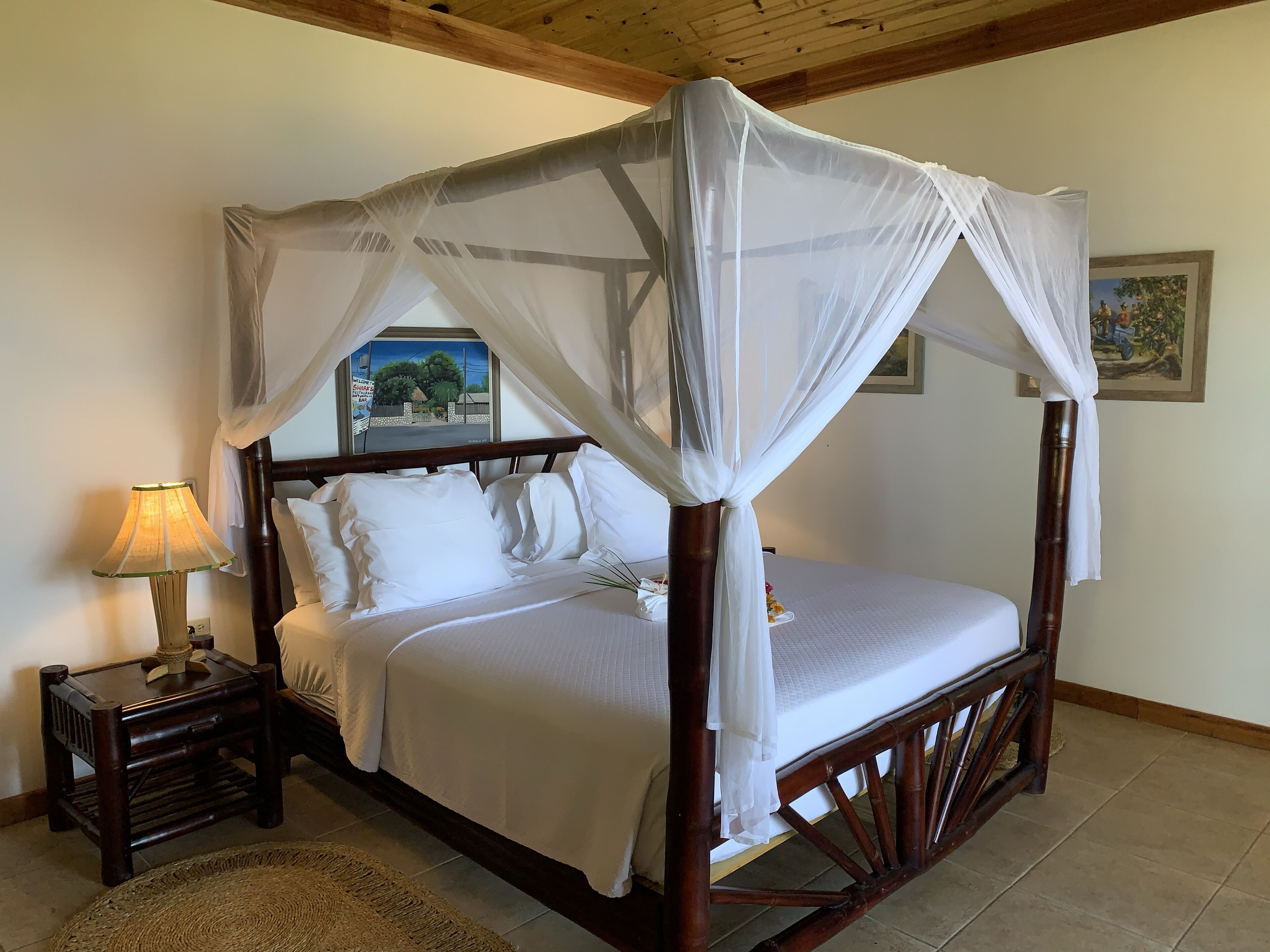 A four-poster bed with a canopy, a bedside table with a lamp, and a framed picture on the wall.