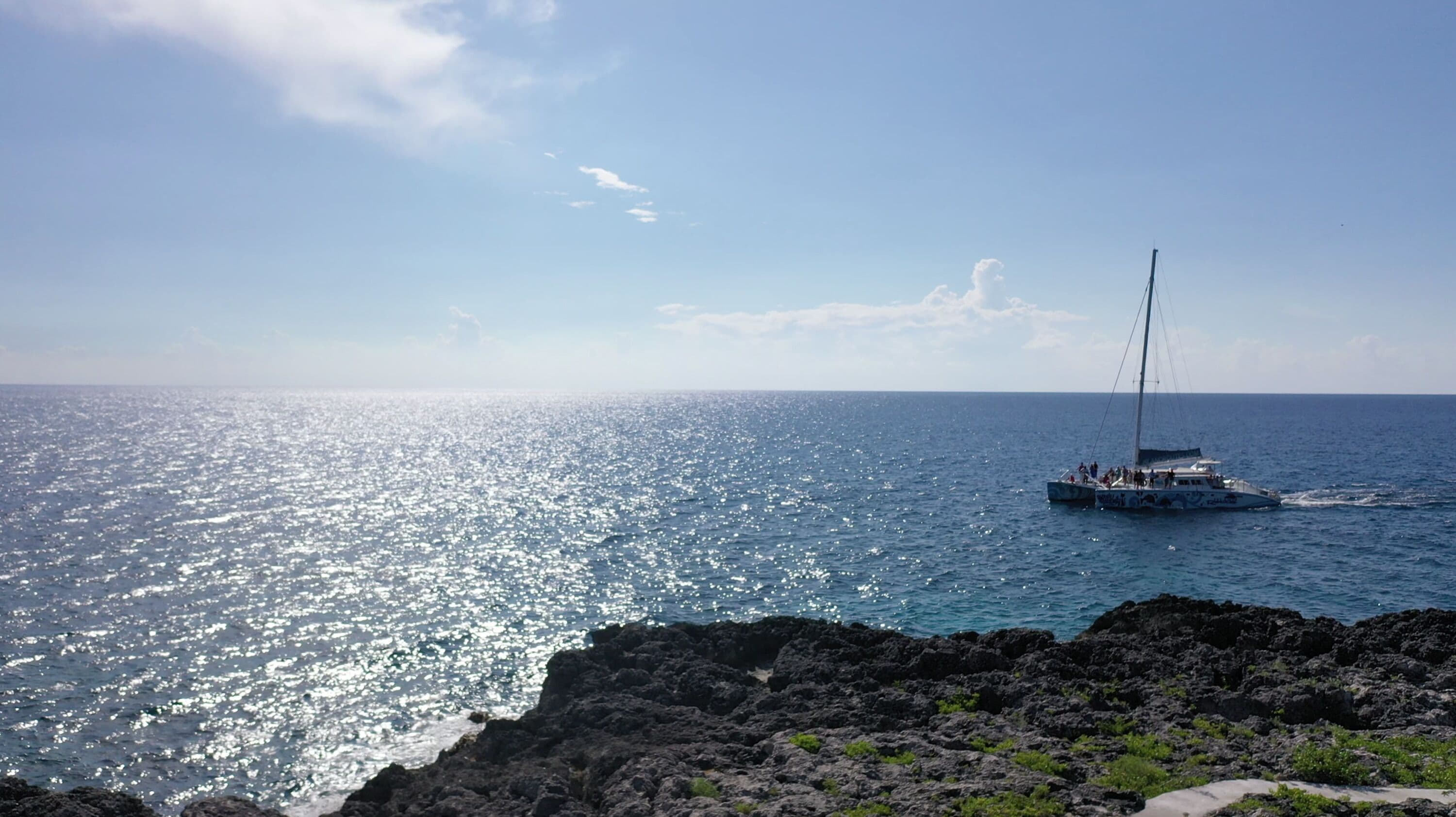 A boat sailing on a calm sea with a rocky coastline in the foreground.