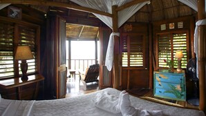 A room with a bed, a wooden nightstand, a chair, and a window with shutters.