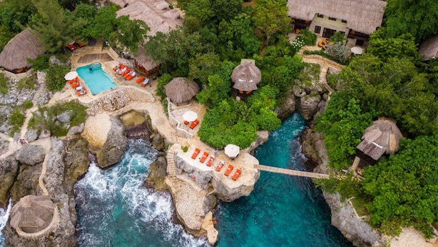 An aerial view of a resort with a swimming pool, lounge chairs, and thatched-roof structures.