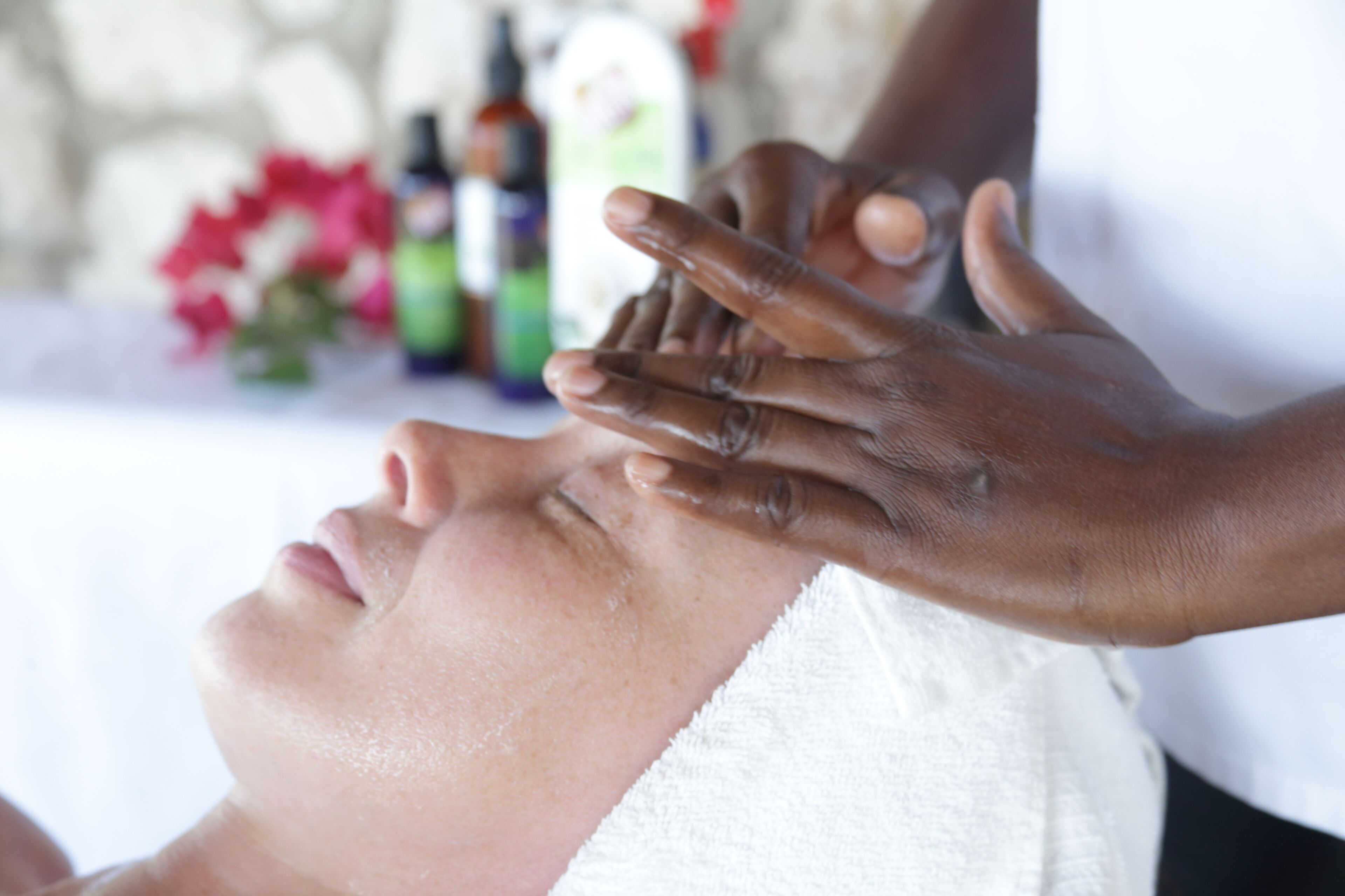 A person receiving a facial treatment with hands applying a substance to the face.