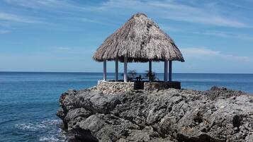 A thatched-roof structure on a rocky outcrop by the sea.