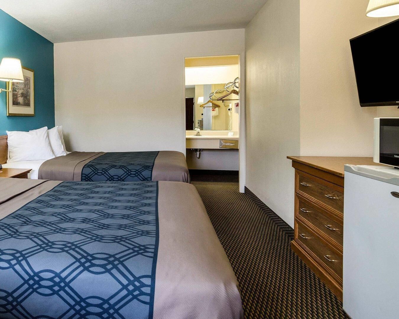 A hotel room with two beds, a dresser, a television, and a mirror.