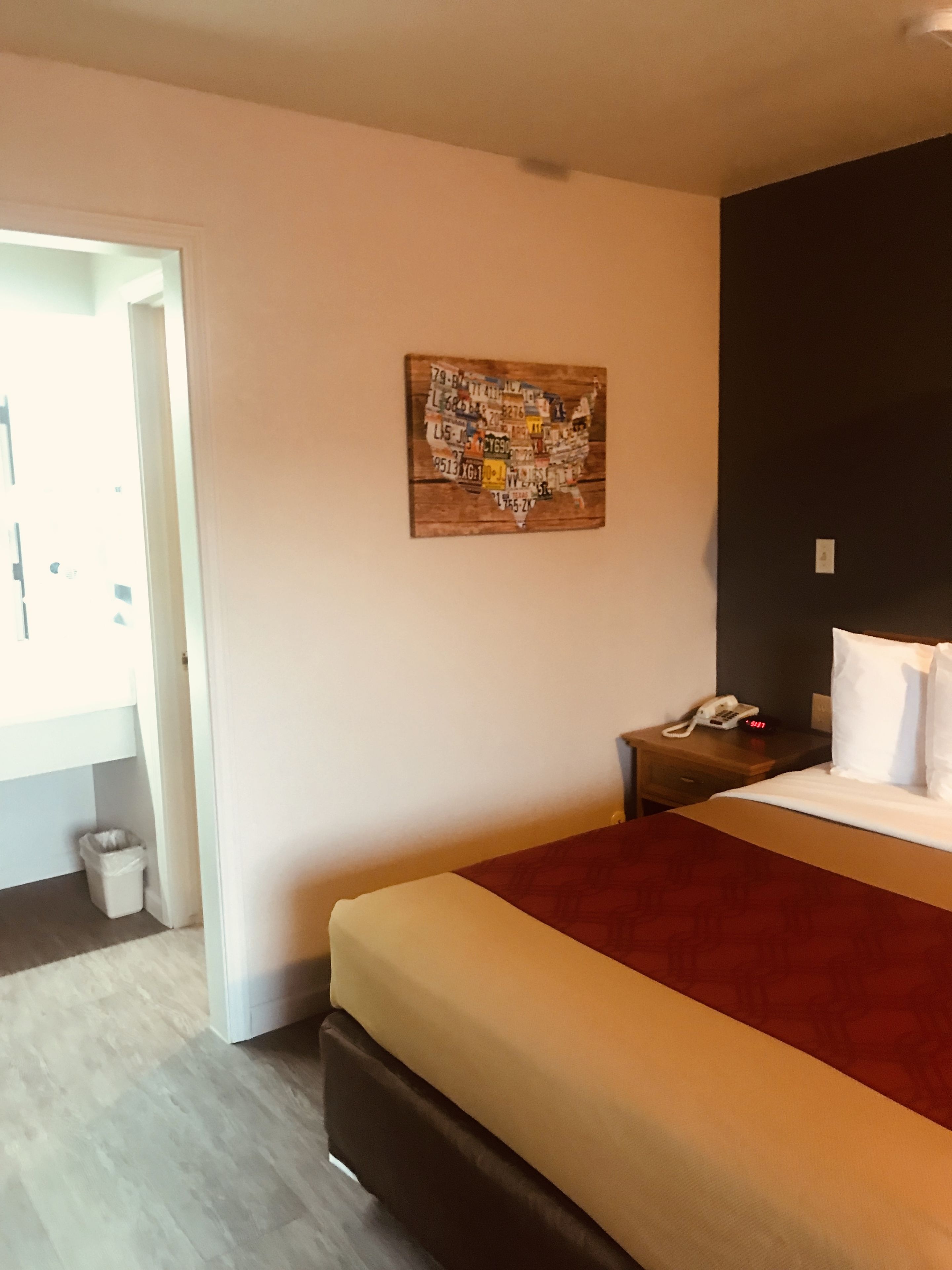 Una habitación de hotel con una cama, una mesita de noche, una obra de arte en la pared del mapa de los Estados Unidos y una puerta que da a otra habitación.