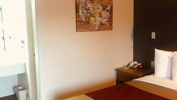 Una habitación de hotel con una cama, una mesita de noche, una obra de arte en la pared del mapa de los Estados Unidos y una puerta que da a otra habitación.